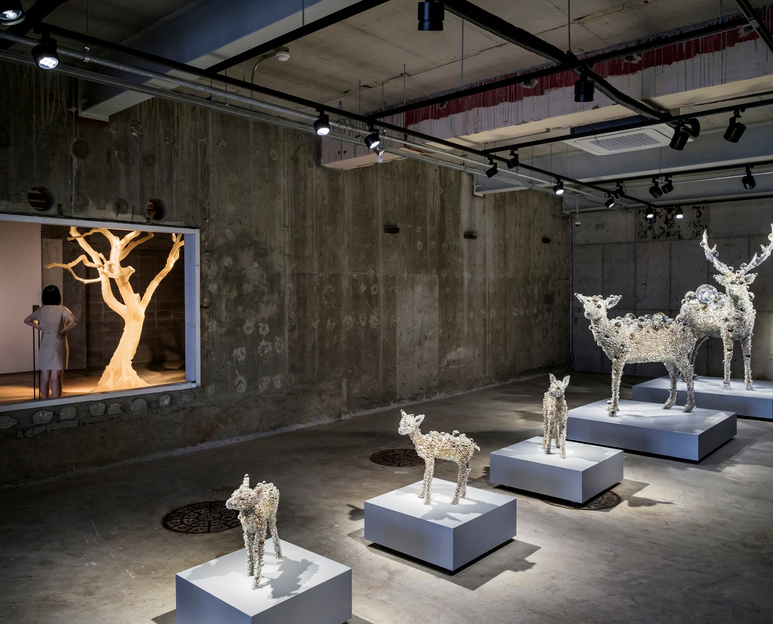 Beleuchtete Kunstausstellung mit Hirschskulpturen und Bauminstallation, akzentuiert durch ERCO-Licht.