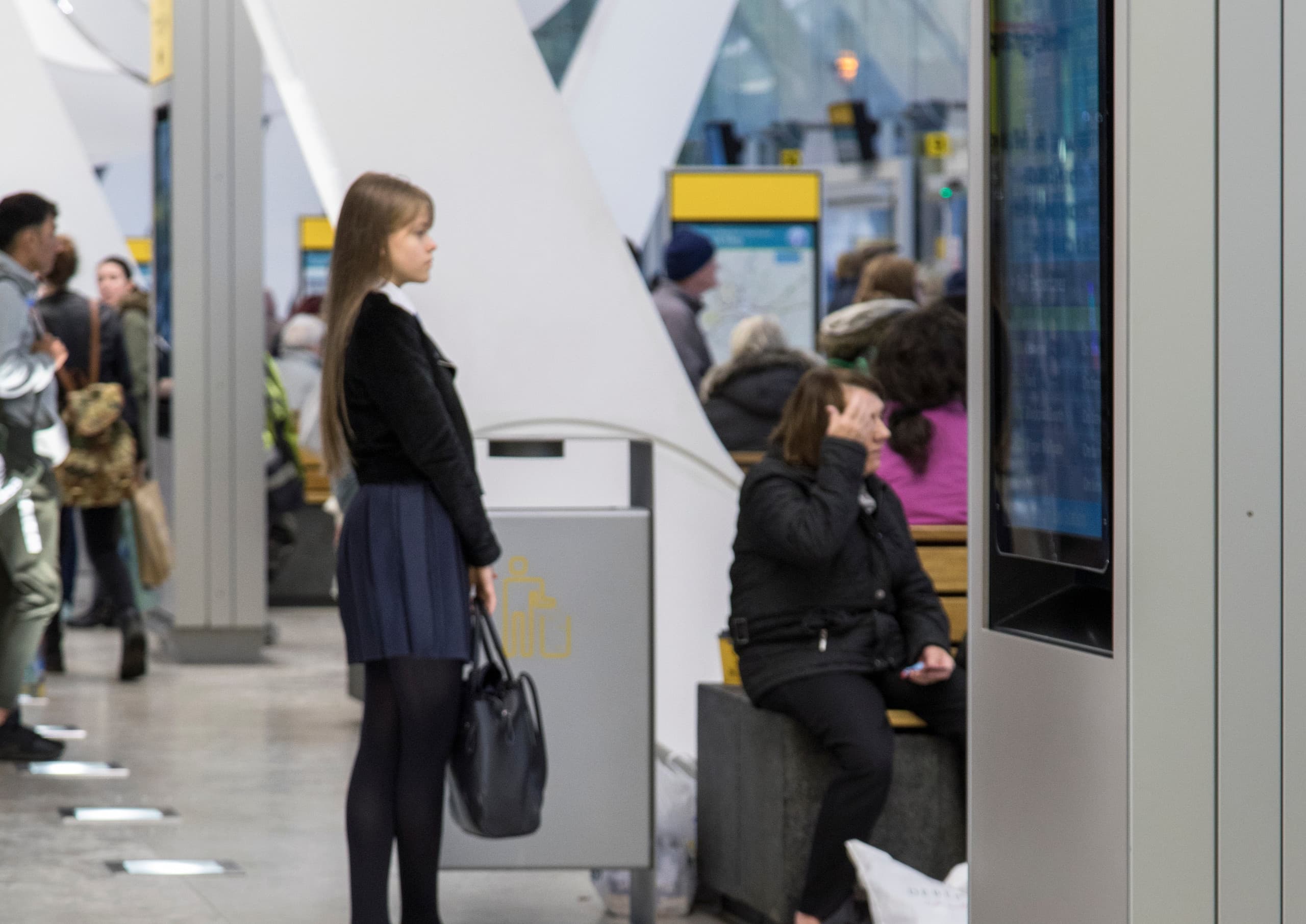 Passagiere warten an einem Bahnhof mit ERCO-Beleuchtung, die Orientierung und Sicherheit bietet.